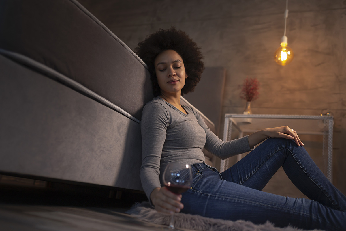 woman sitting on floor drinking wine showing women and alcoholism