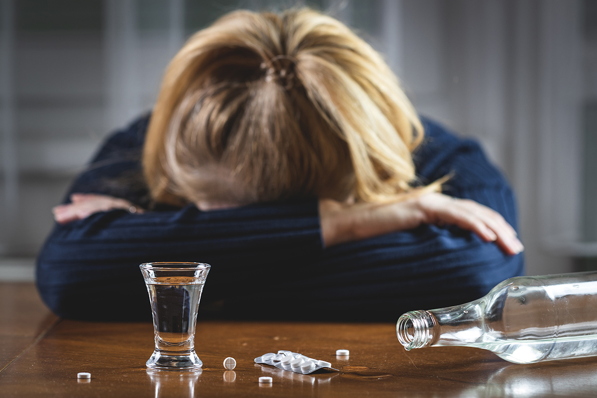 woman with head down next to alcohol and drugs from Dangers of Mixing Substances