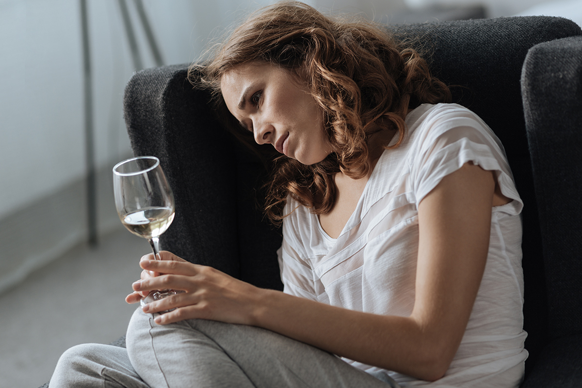 woman curled up on chair staring at wine questioning Is Alcohol a Depressant